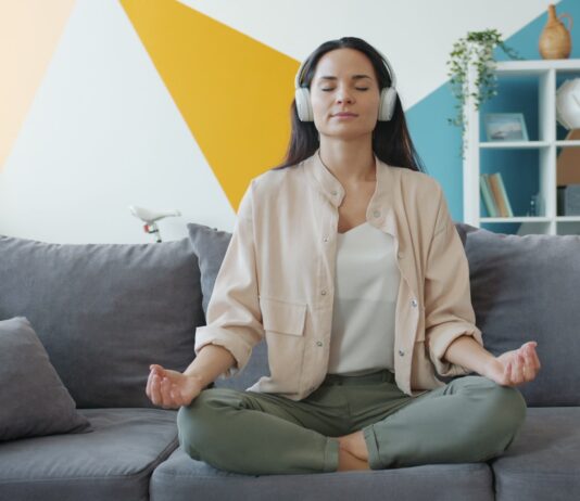 변화하는 정신건강 트렌드, ‘마음 챙김’이 일상 속으로 Woman meditating on couch with headphones on