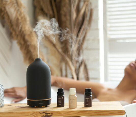 집에서 실천하는 ‘대체요법’, 건강한 일상 위한 새로운 트렌드 a woman laying in a bathtub next to a bottle of essential oils