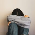 “담배 15개비보다 해롭다”… 당신을 서서히 죽이는 보이지 않는 전염병 ‘외로움’ a woman sitting on the floor with her arms wrapped around her head